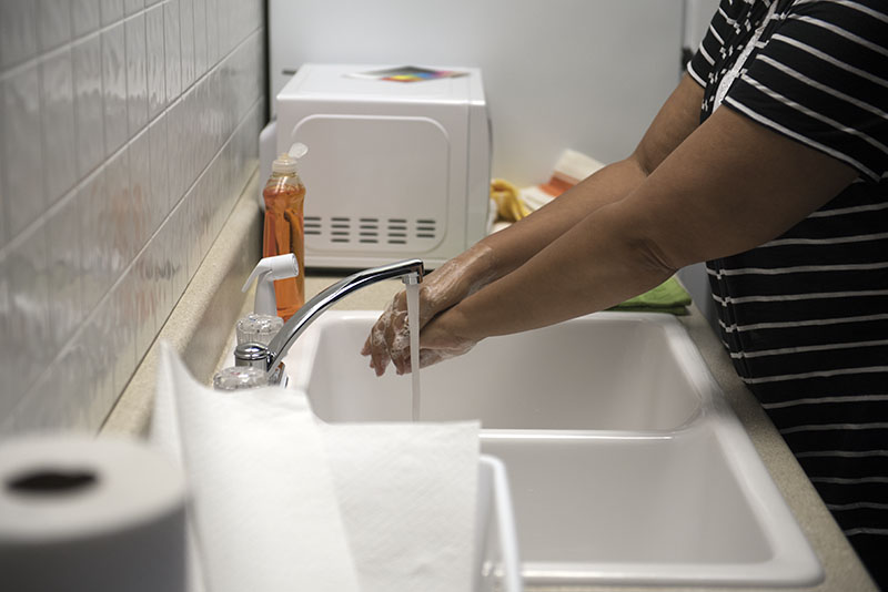 A woman washes to soap from her hands at a sink using running water.