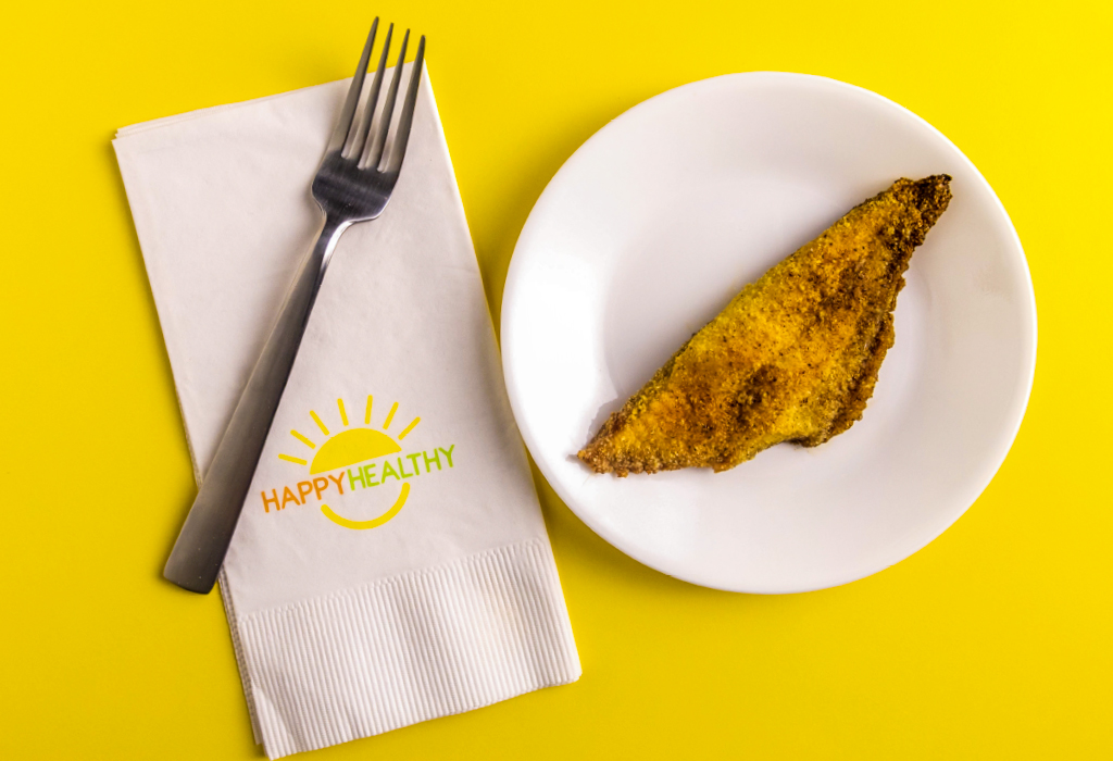 Fork and napkin beside plate with a cooked, seasoned catfish fillet