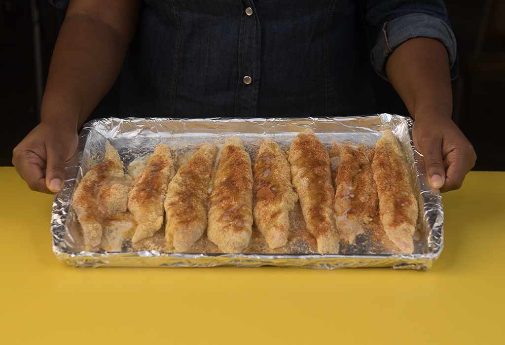 hands holding foil wrapped backing sheet with 8 pieces of seasoned meat