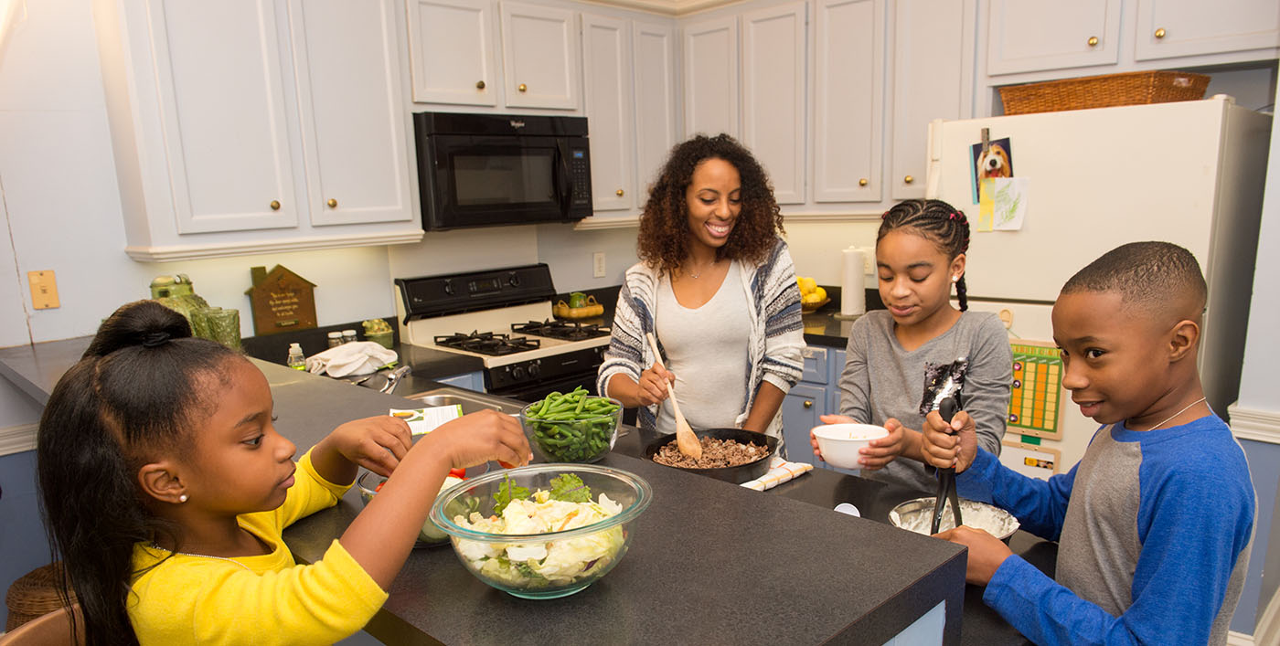 A family prepares a healthy dinner, green salad, green beans, ground beef and mashed potatoes, together. 
