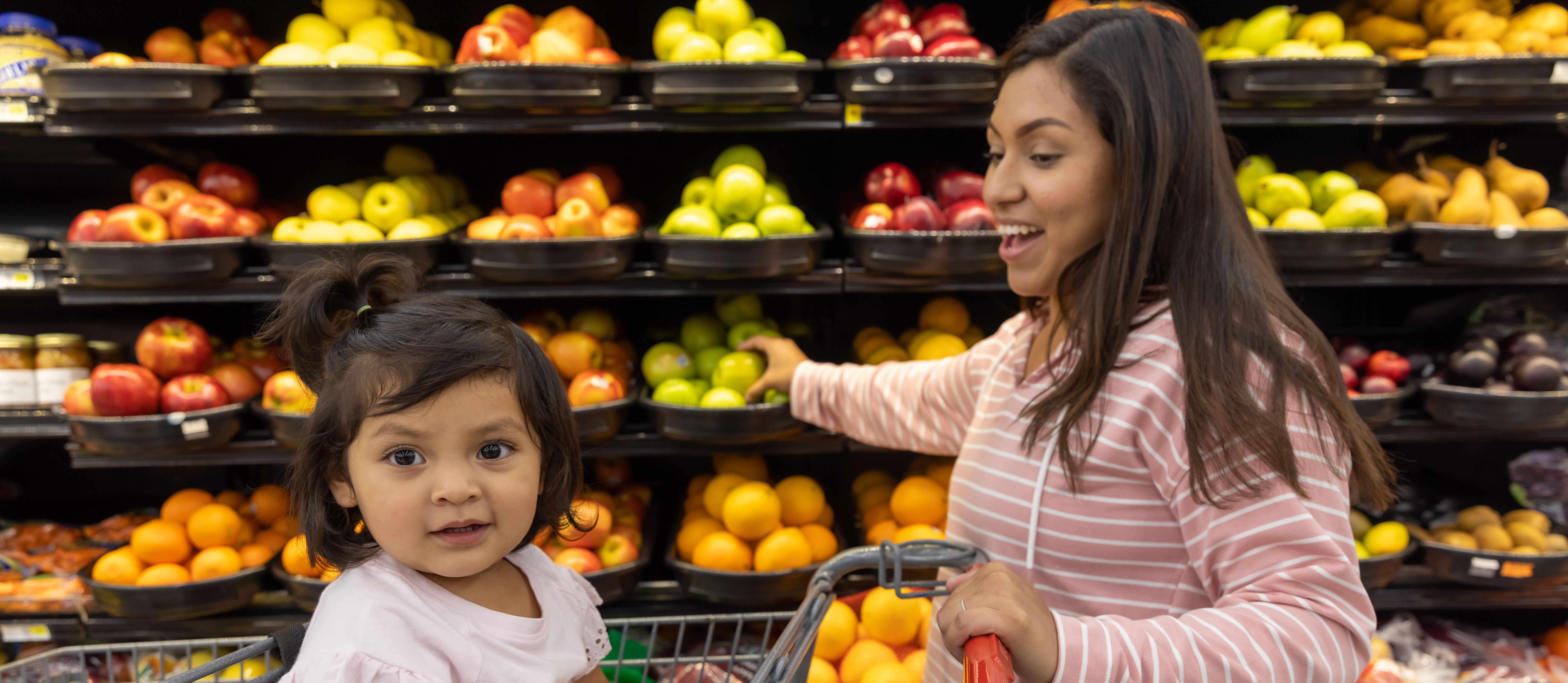 A woman and young girl shop for fruit in a grocery store.