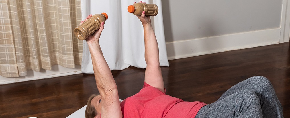 A woman exercising on the ground lifting weighted bottles