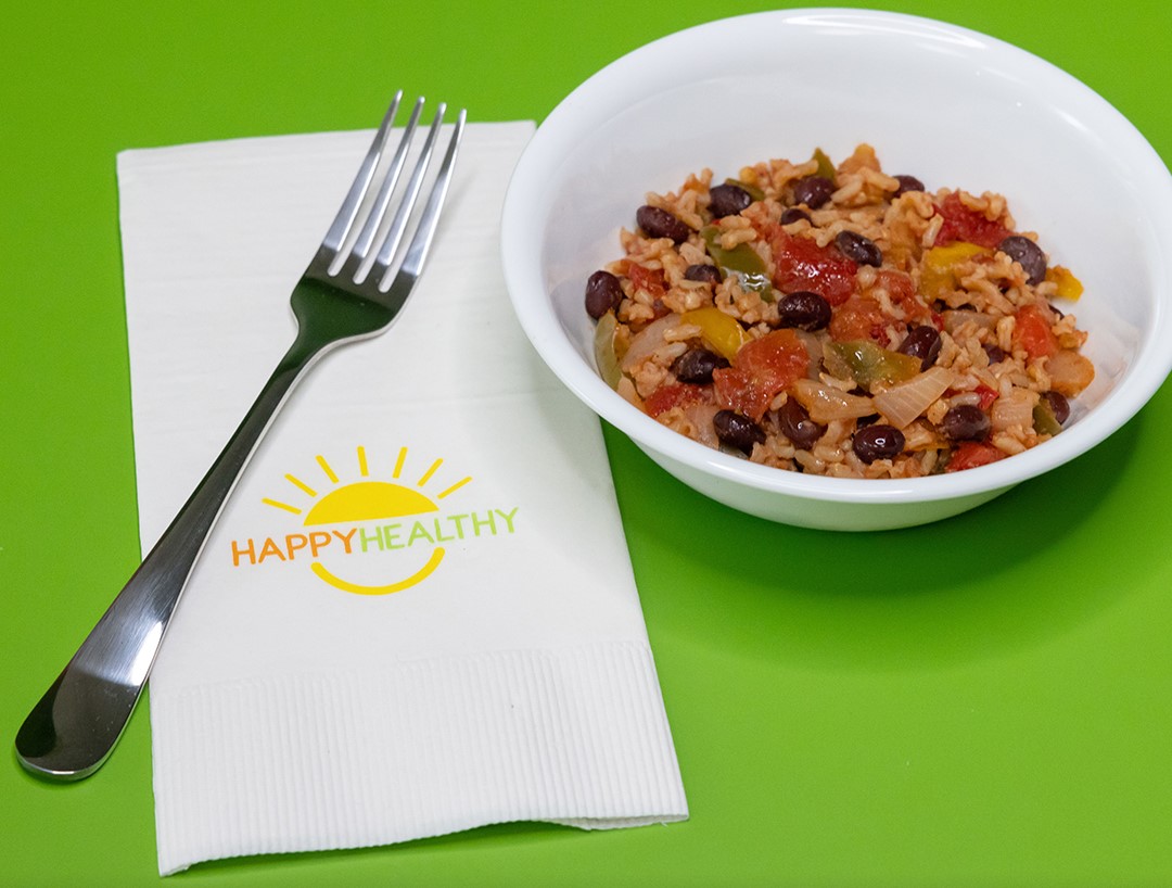 A white bowl of Black Beans and Rice on a green background next to a fork and napkin