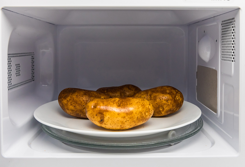 4 potatoes on white plate in microwave.