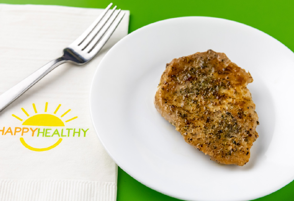 Baked Pork Chop on white plate next to white HappyHealthy napkin and fork