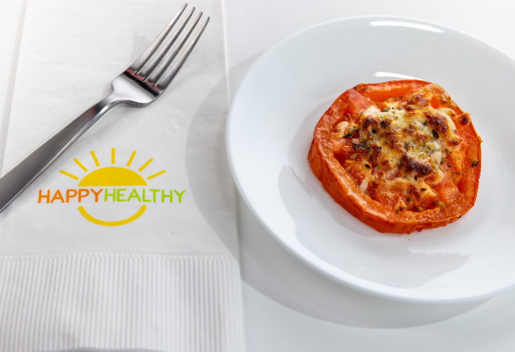 A plate with one baked tomato next to a fork and Happy Healthy napkin