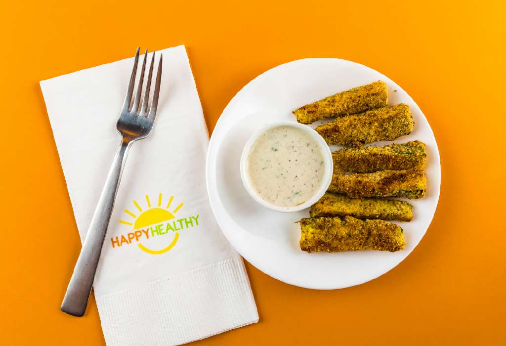 Plate with zucchini sticks and cup of low-fat ranch dressing beside a napkin and fork.