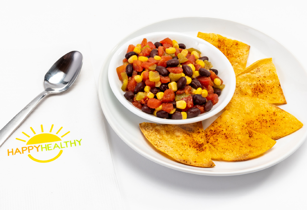Black Bean and Corn Salsa in white bowl on white plate with chips, next to HappyHealthy napkin and spoon
