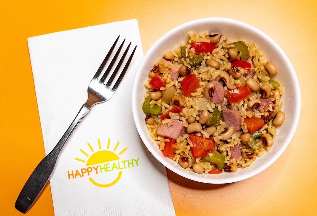 A white bowl filled with black eyed peas and rice next to a fork and HappyHealthy napkin