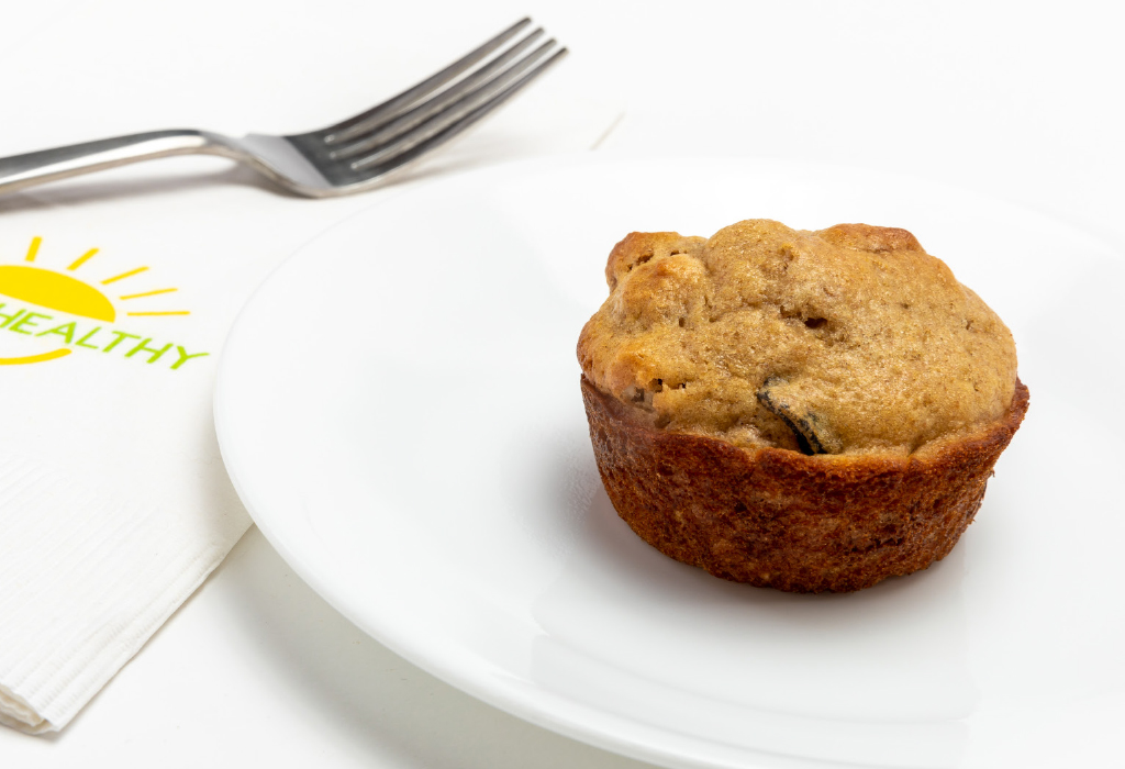 Bran muffin on white circle plate next to HappyHealthy napkin and fork