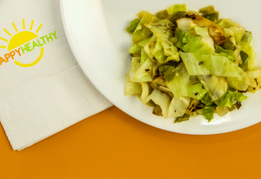 A plate filled with a serving of cabbage stir-fry with a HappyHealthy napkin to the side.