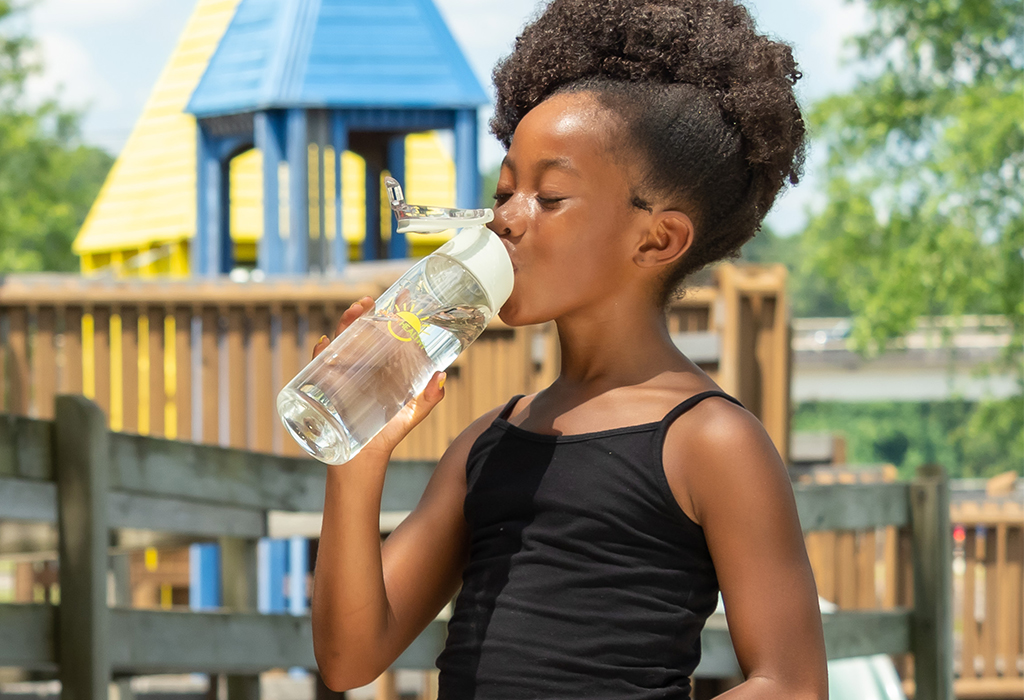 Girl on a playground drinking water from a bottle.