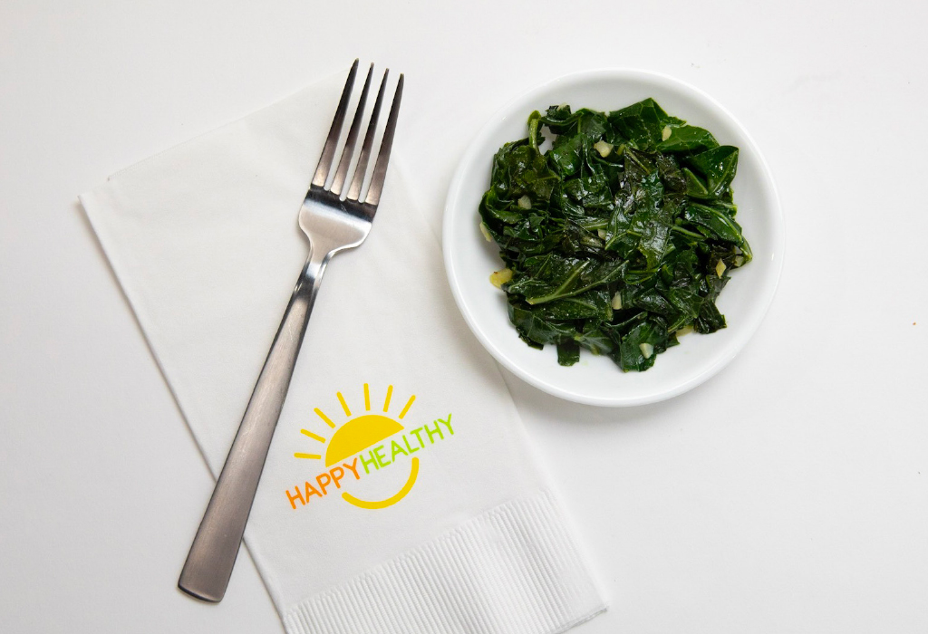 Plate of collard greens beside napkin and fork.