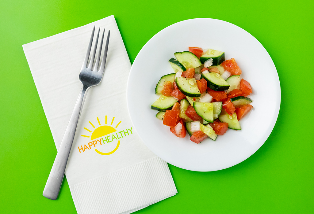 Cucumber and Tomato Salad on white plate next to HappyHealthy napkin and fork