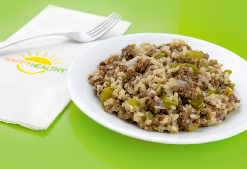 A white plate full of dirty rice on a green background next to a fork and HappyHealthy Napkin