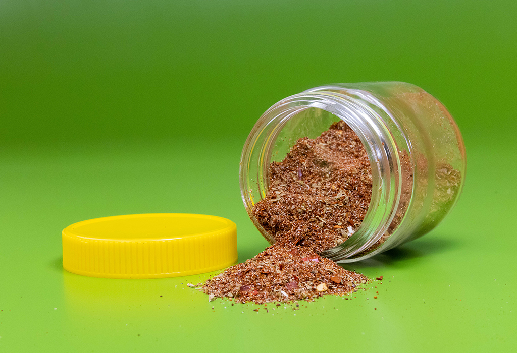 An open jar on its side spilling taco seasoning onto a green table