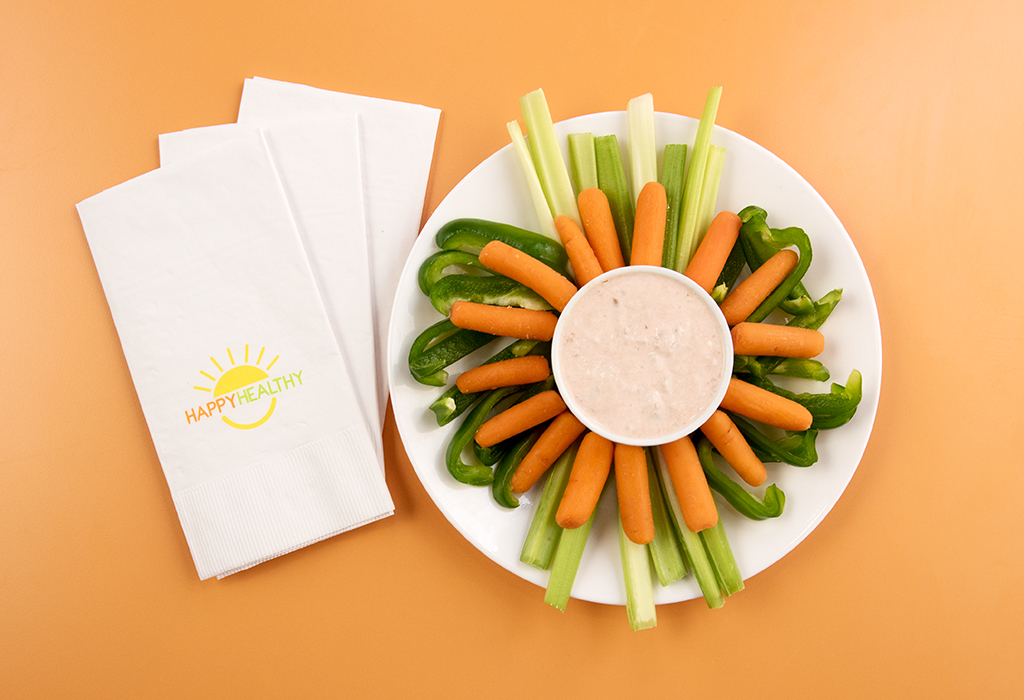 Plated fresh vegetables: baby carrots, celery, and bell peppers surrounding a bowl of sour cream and salsa dip.