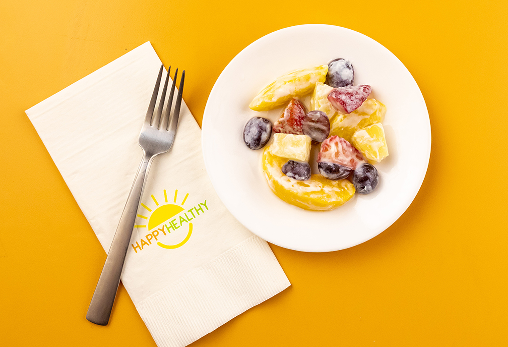 Creamy Fruit Salad on white plate next to HappyHealthy napkin and fork