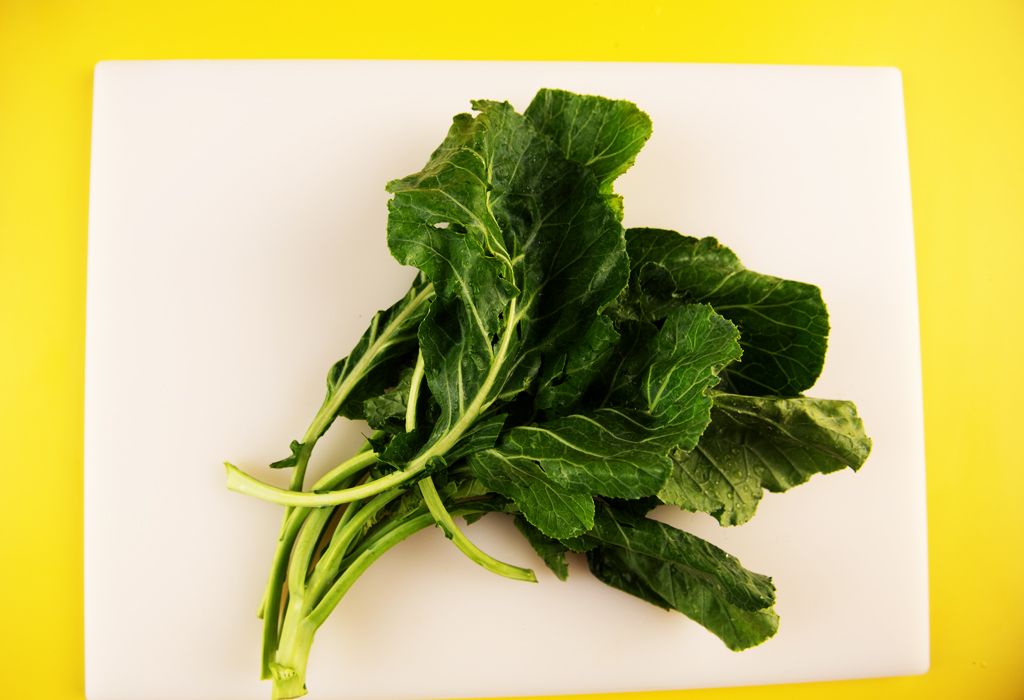 Fresh leafy greens placed on white cutting board with yellow background. 