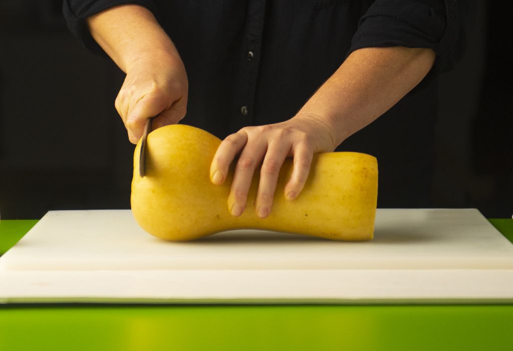 Woman cutting winter squash on a cutting board. 