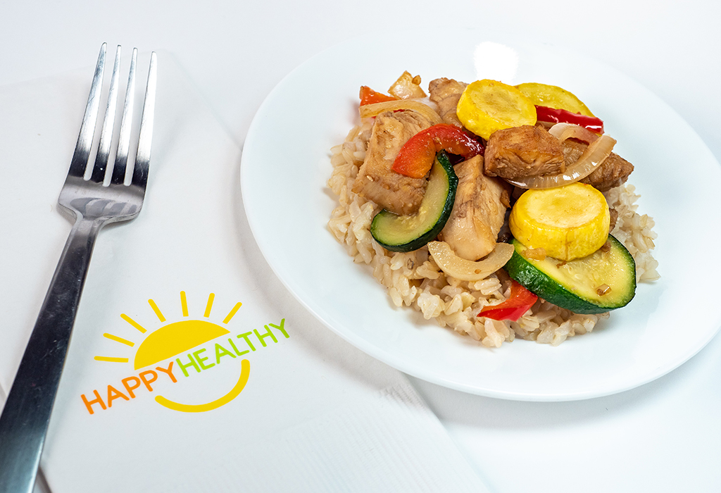 A plate of stir fry with chicken, squash, onion, peppers and rice
