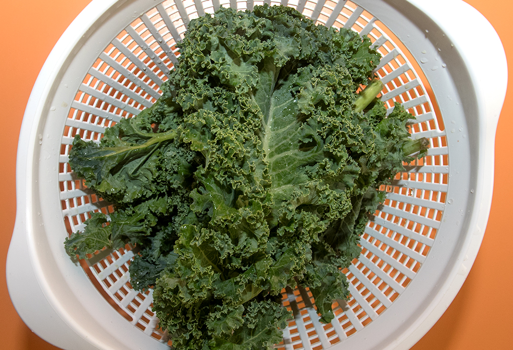 Rinsed greens in a white colander with an orange background. 