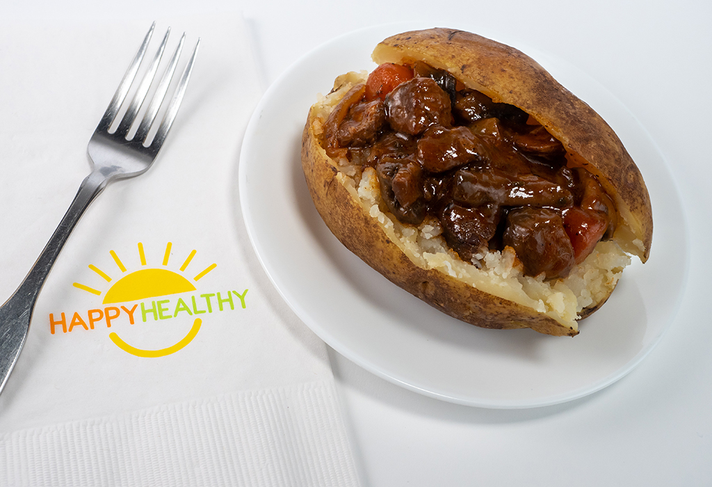 A baked potato topped with beef stew next to a fork and HappyHealthy napkin