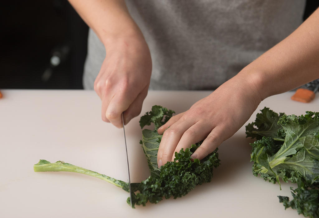 Hands using knife to cut stems off of leafy greens