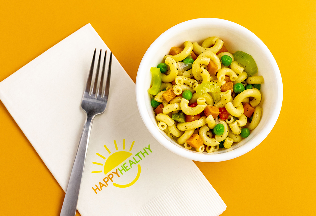 Macaroni Salad in white bowl next to HappyHealthy napkin and fork.