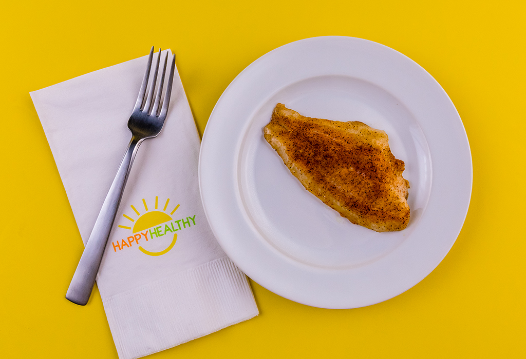 Fillet of Oven Blackened Catfish on white plate next to HappyHealthy napkin and fork