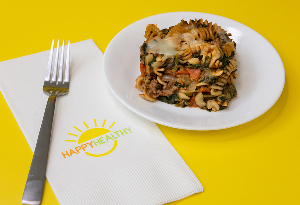 a plate of pizza casserole on a yellow background next to a HappyHealthy napkin and fork