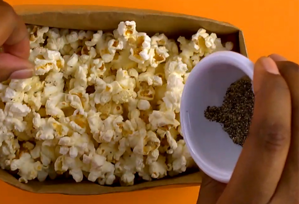 Bag of popcorn with hand adding seasoning