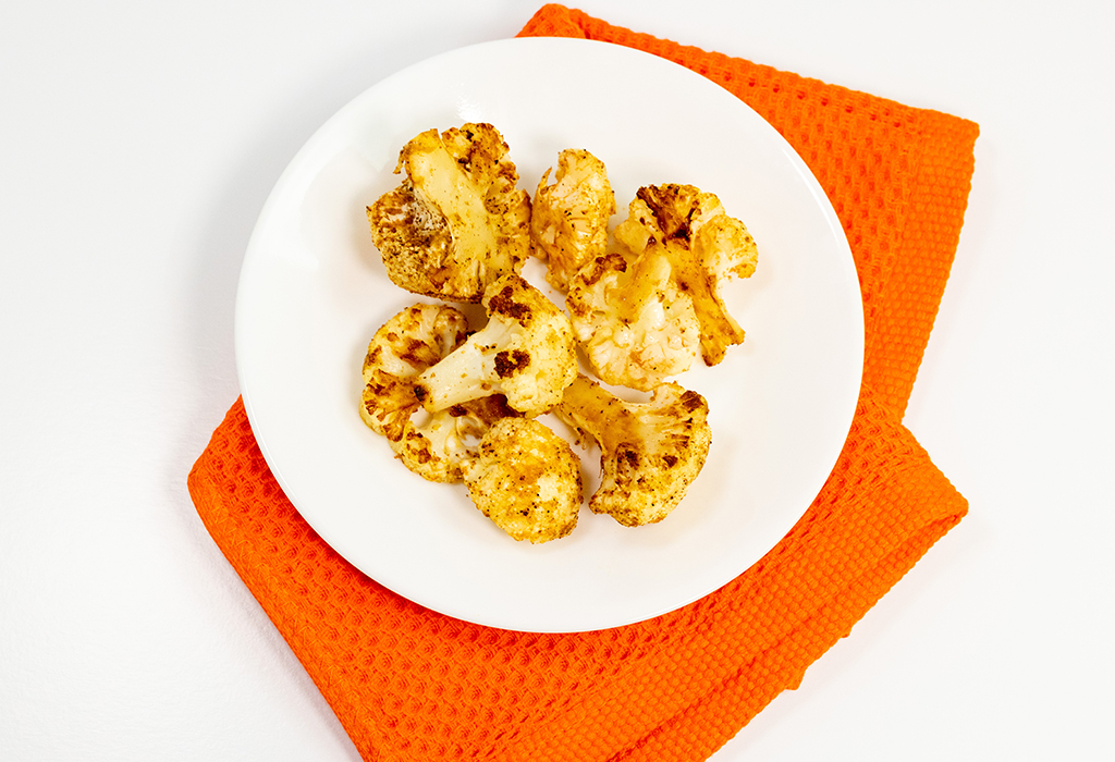 A bowl of Roasted Cauliflower on an orange cloth on a white background