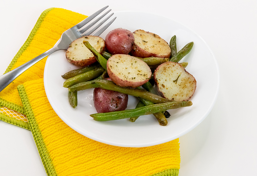 A white plate of Roasted Green Beans and Red Potatoes on a yellow cloth napkin