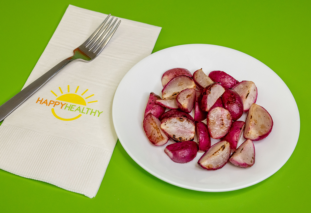 a plate of Roasted Radishes on a green background next to a HappyHealthy napkin and fork