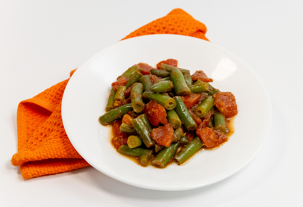 A white bowl of Sautéed Green Beans on top of an orange napkin on a white background