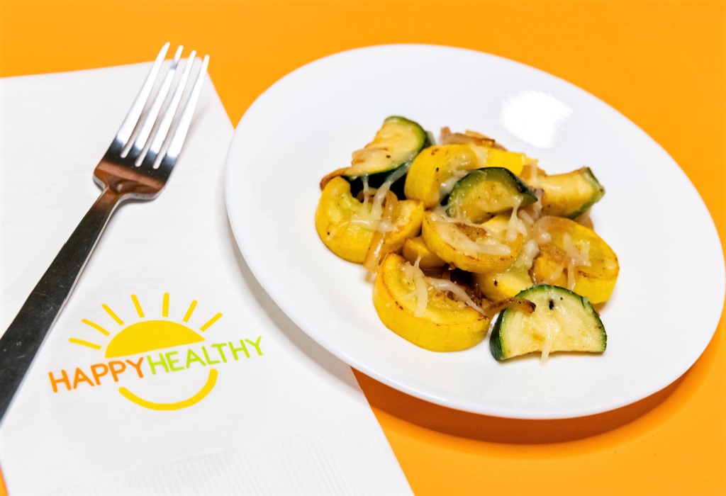 A white plate with sauteed squash next to a fork and HappyHealthy napkin