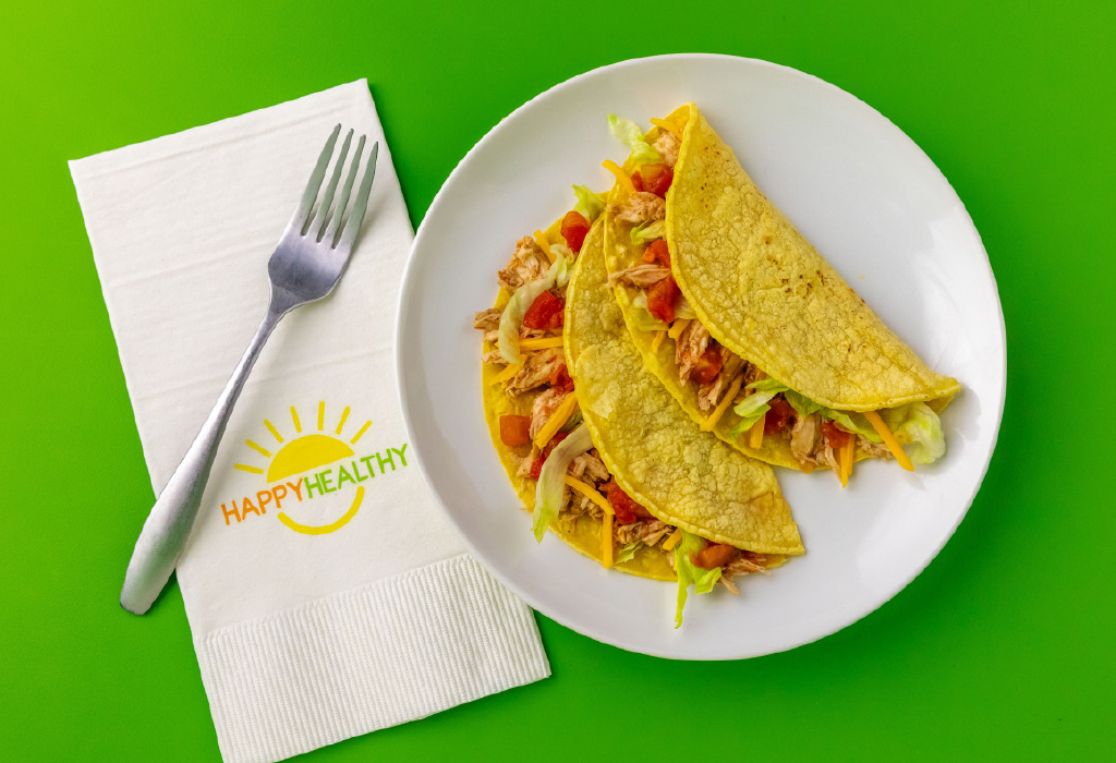 Two Slow Cooker Chicken Tacos on white plate next to HappyHealthy napkin with fork