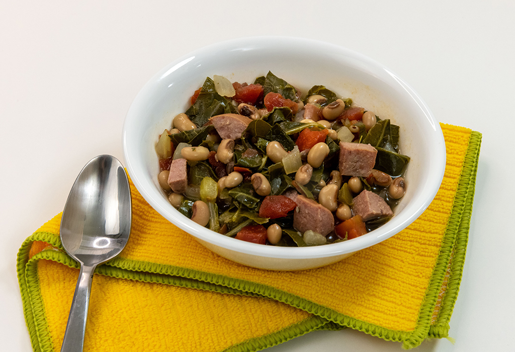 A bowl of Slow Cooker Sausage, Greens, and Black-eyed Peas on a yellow napkin