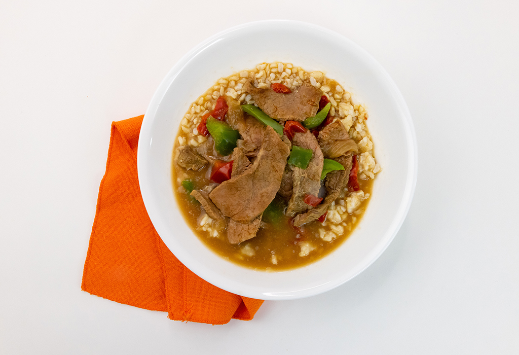 A white bowl filled with Slow Cooker Steak and Peppers next to an orange napkin