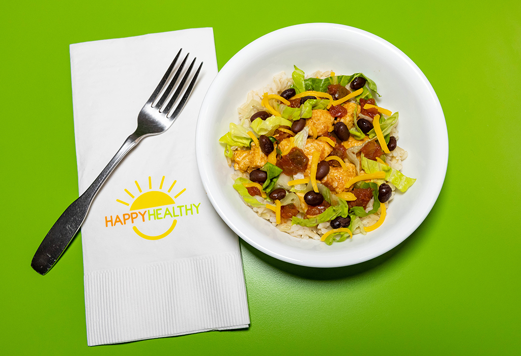 A southwest bowl with rice, chicken, lettuce, black beans, salsa, cheese next to a fork and HappyHealthy napkin