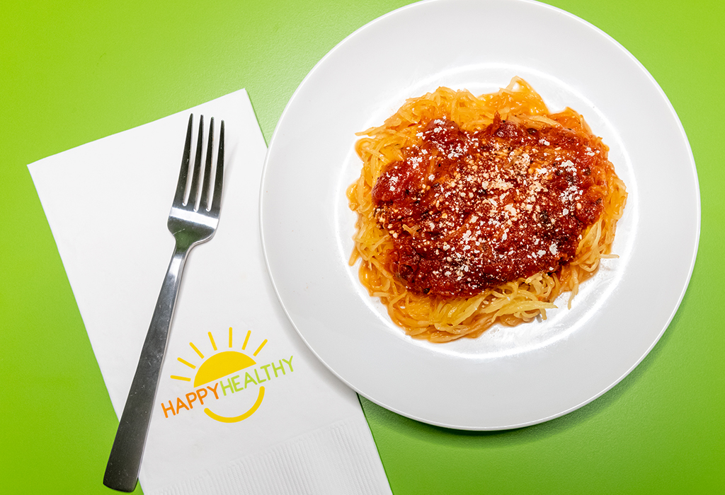 A white plate of Spaghetti Squash with Tomato Sauce next to a fork and HappyHealthy napkin