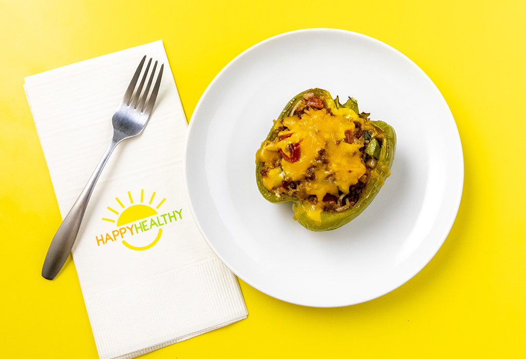 A stuffed bell pepper on a white plate next to a Happy Healthy Napkin and Fork