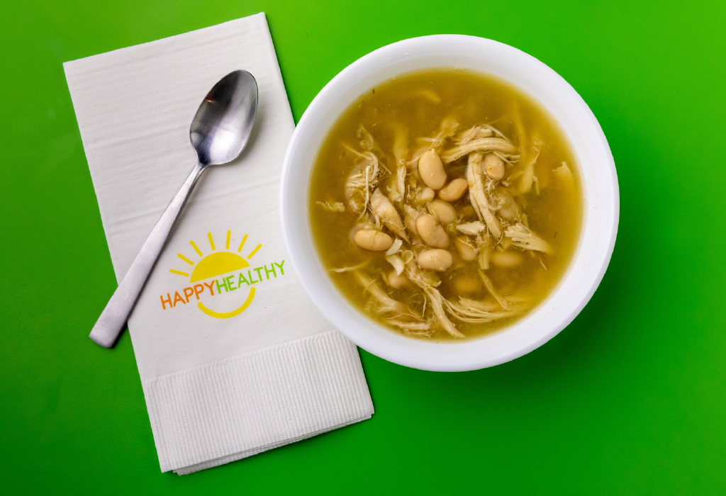 White chicken chili in white bowl next to HappyHealthy napkin and spoon.