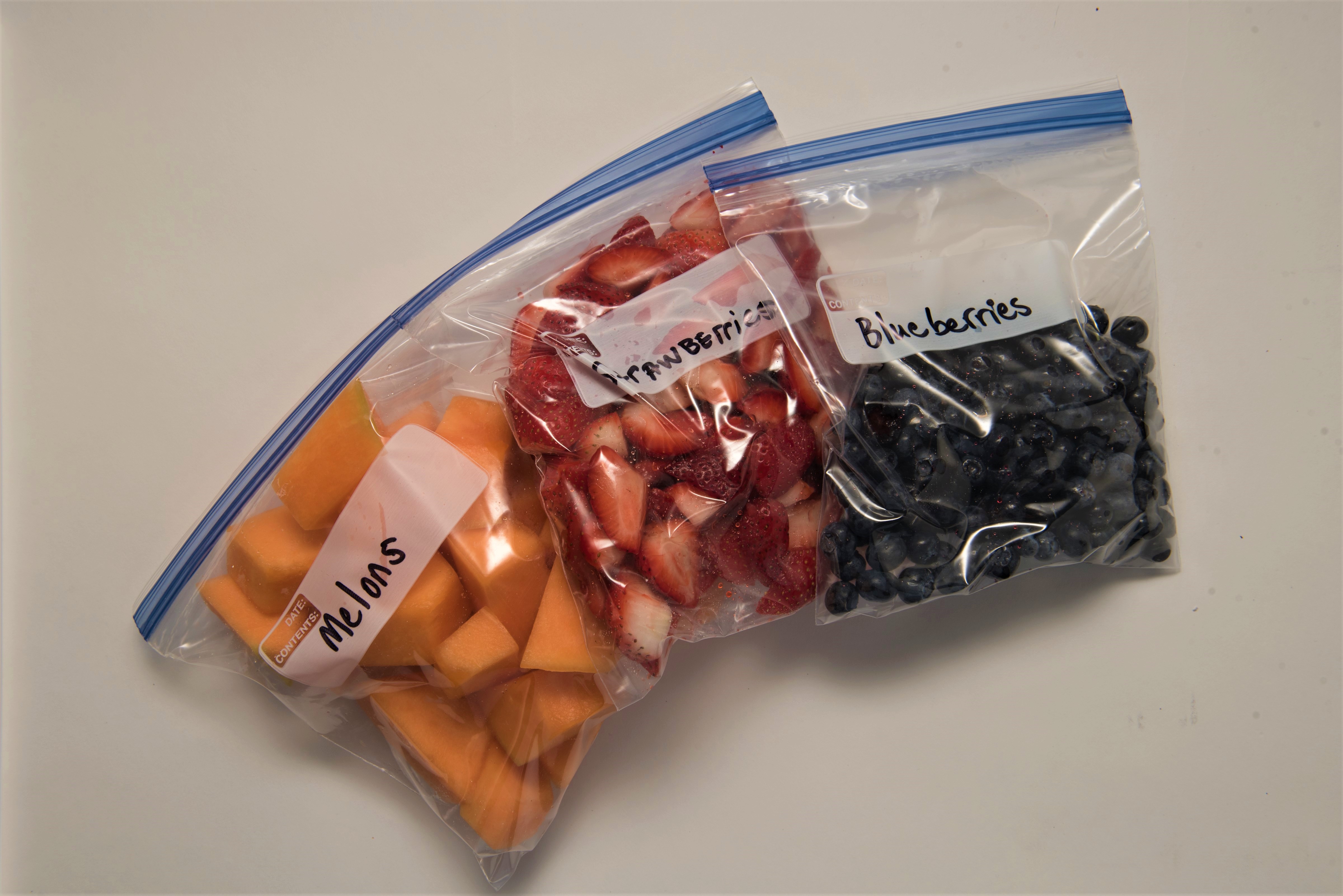 Sliced mango, sliced strawberries, and blueberries in plastic bags for storage.