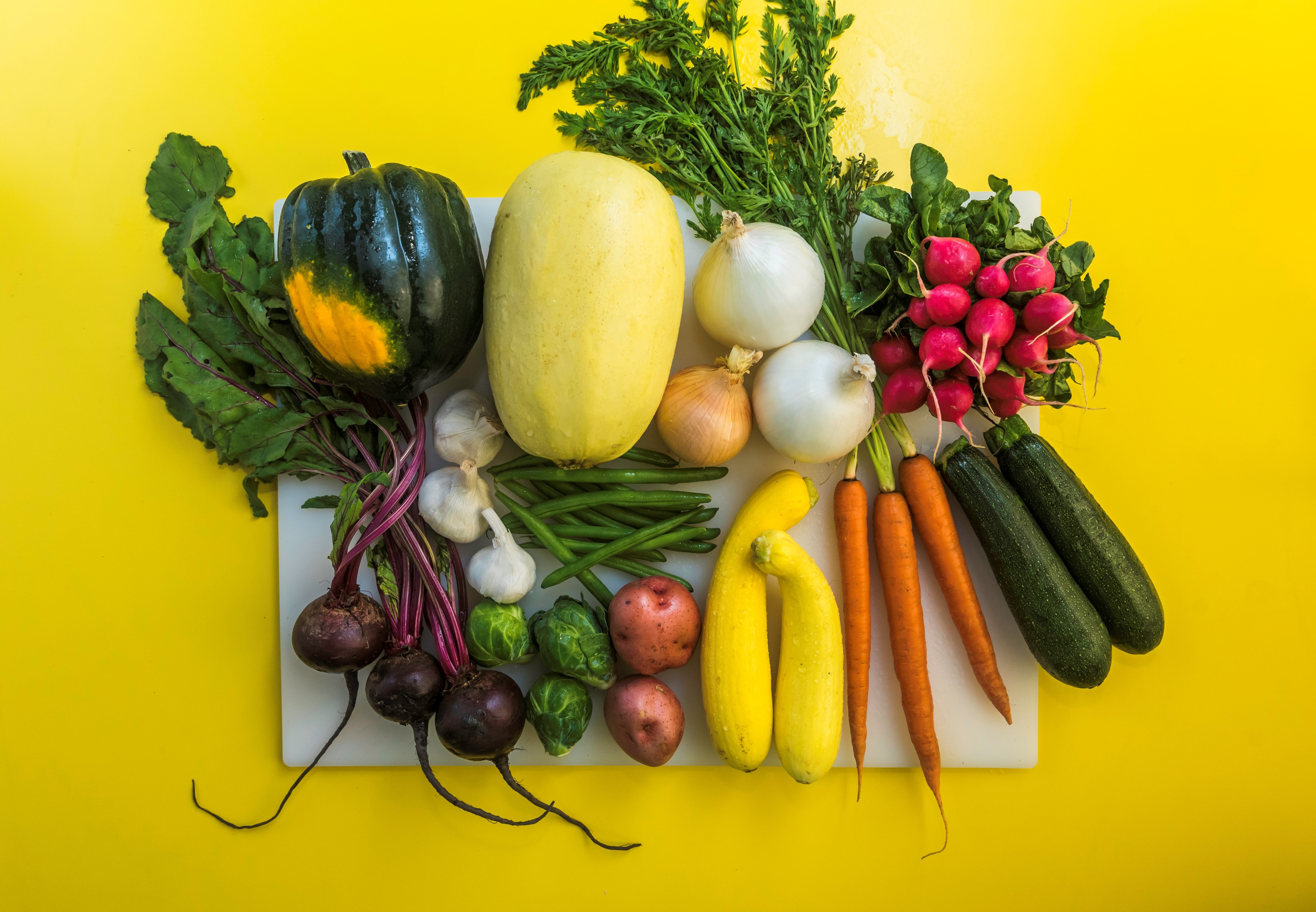 Variety of vegetables on white cutting board (carrots, squash, beets, onions, cucumber)