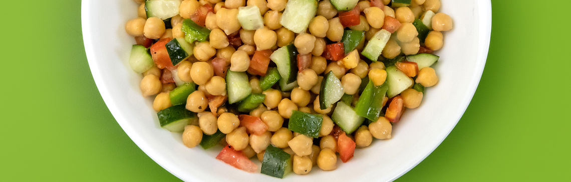 A white bowl of chickpea salad on a green background