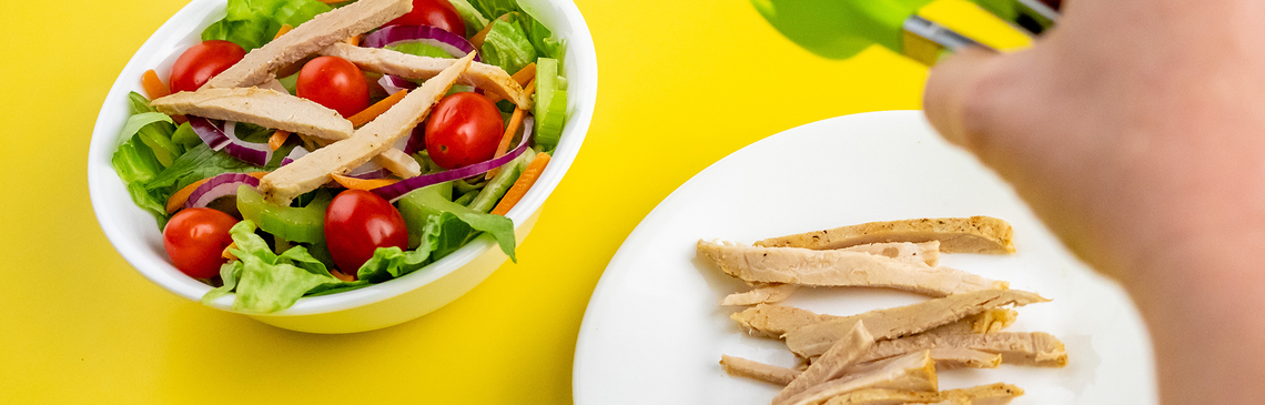 A plate of chicken strips, a bowl of salad and a hand with tongs over the chicken