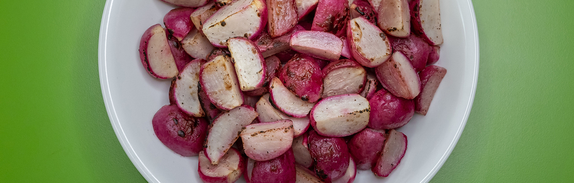 a bowl of roasted radishes on a green background