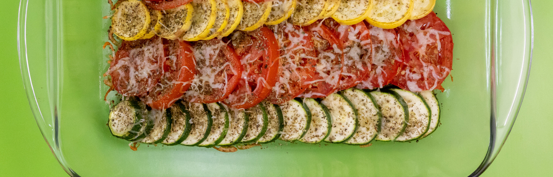 A casserole dish of tomatoes, squash and zucchini on a green background